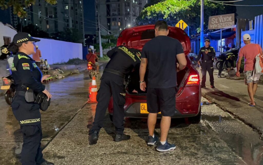Agentes de la Policía Metropolitana inspeccionan el baúl de un vehículo en un punto de control nocturno en Cartagena. 