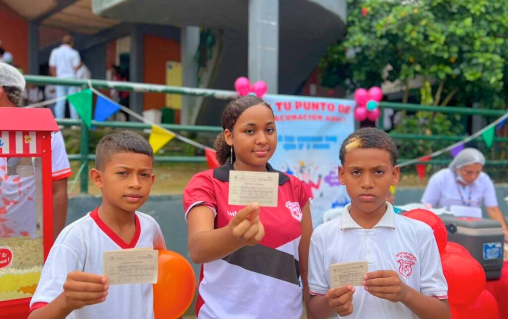 Tres niños muestran sus carnés actualizados en un punto escolar durante la Jornada de Vacunación en Cartagena.