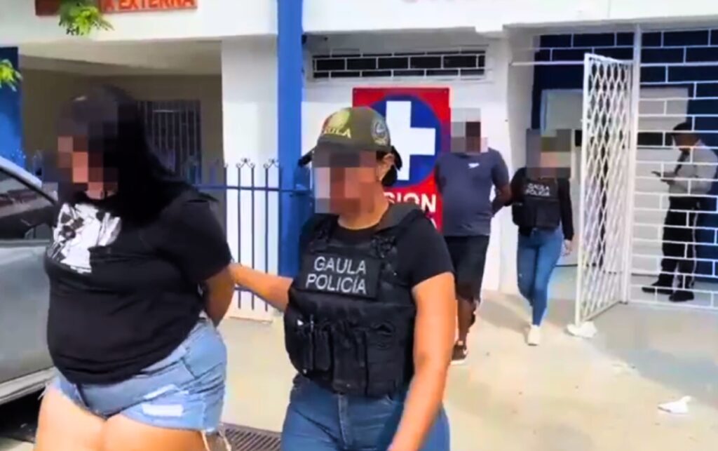 Capturan a 4 presuntos extorsionistas_ funcionaria del GAULA escolta a una mujer detenida con el rostro pixelado frente a un centro asistencial.