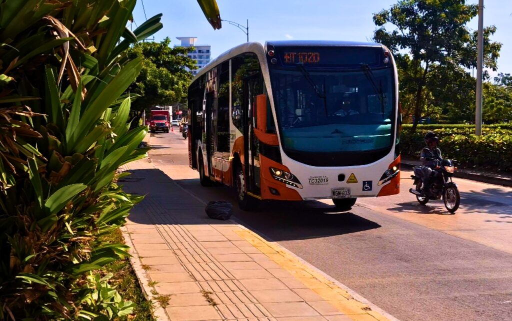 Bus articulado de Transcaribe acercándose a un paradero mientras motos pasan a su lado en una vía de Cartagena.