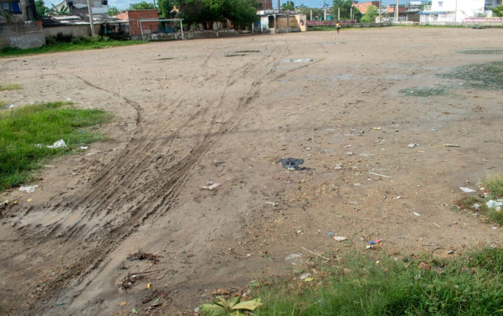 Terreno del campo deportivo con maleza alta y zonas irregulares.