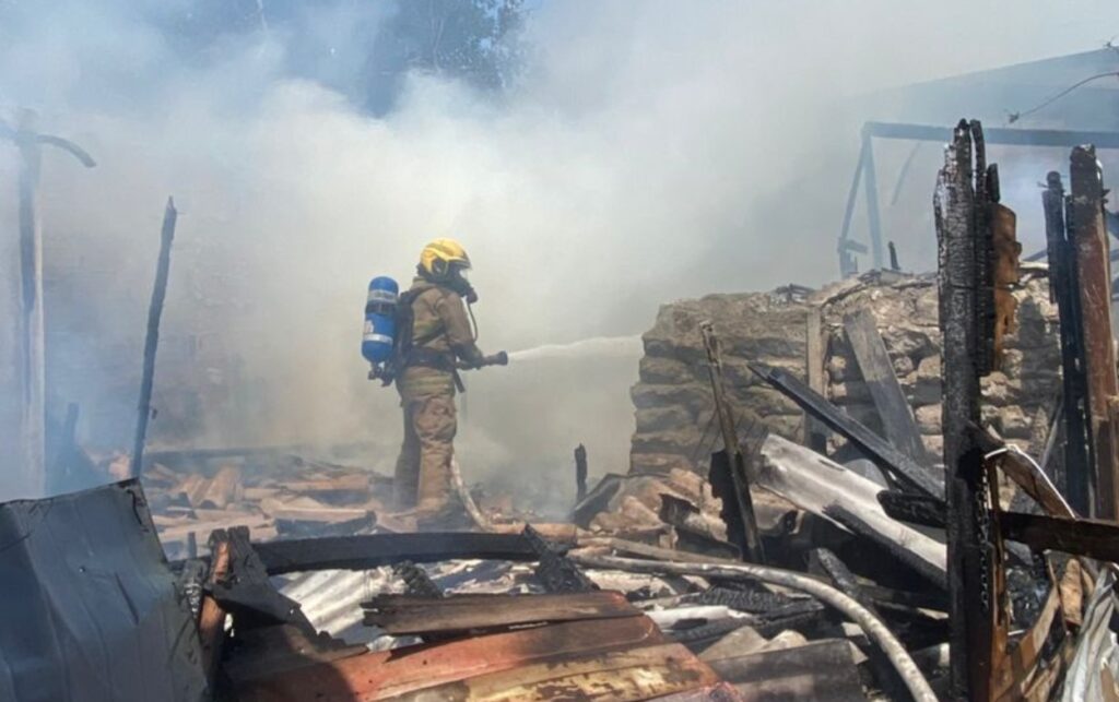 Escena de devastación tras incendio que dejó 4 viviendas afectadas en Cartagena, con bomberos controlando las llamas entre restos calcinados. 