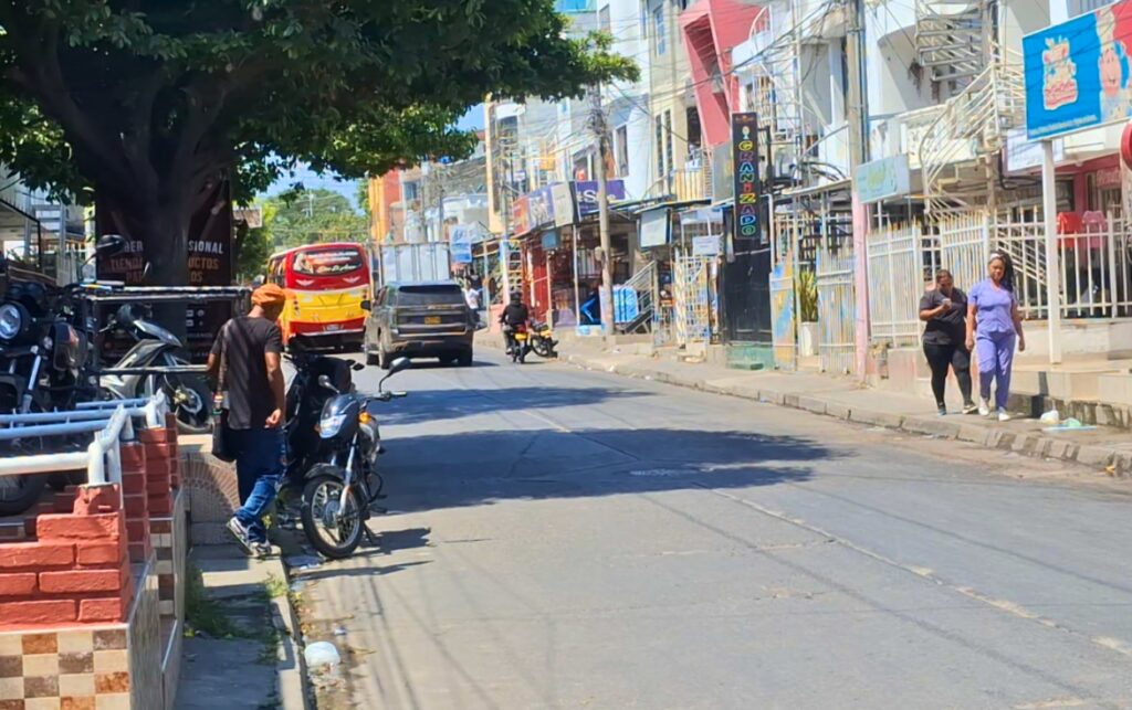 Denuncian irregularidades en el barrio El Campestre, vista de calle comercial con tránsito de peatones y motocicletas en jornada previa a elecciones comunales.