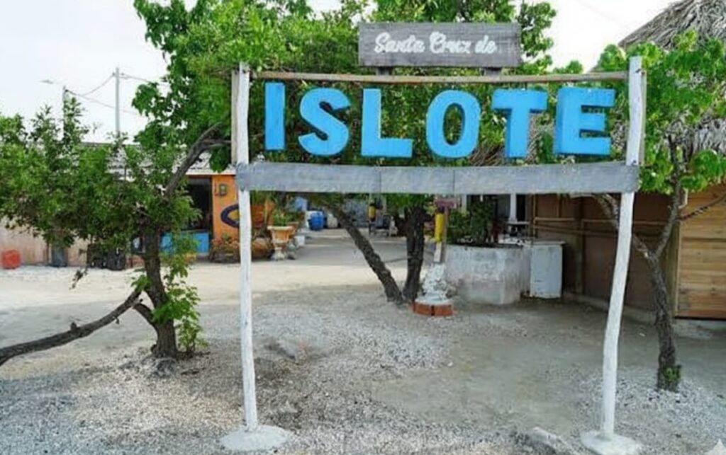 Entrada principal al Islote zona donde ejerce el funcionario en riesgo extremo, con el letrero “Santa Cruz del Islote” rodeado de viviendas y senderos peatonales de arena.