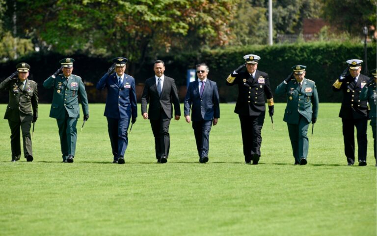 Filas de altos mandos militares caminando en formación junto al presidente Gustavo Petro y otro funcionario, sobre una explanada verde
